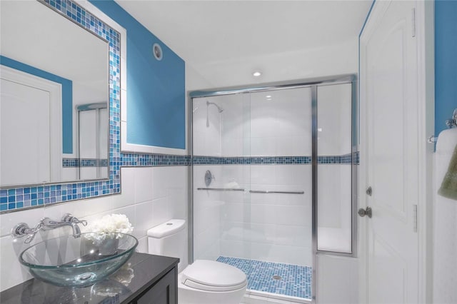 bathroom with vanity, a shower with shower door, tile walls, and toilet