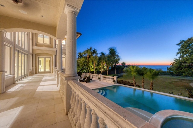 pool at dusk with an in ground hot tub, a patio, and french doors