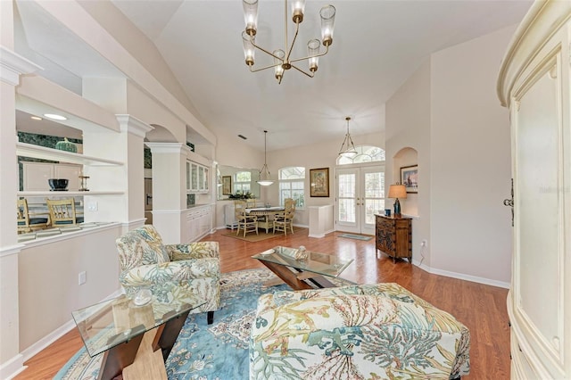 living room featuring french doors, ornate columns, vaulted ceiling, a notable chandelier, and light hardwood / wood-style floors