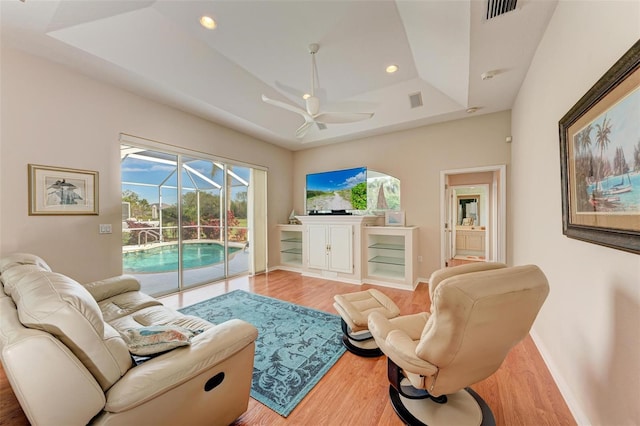 living room with ceiling fan, light hardwood / wood-style floors, and a raised ceiling