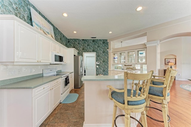 kitchen with a breakfast bar, white appliances, decorative columns, and white cabinetry