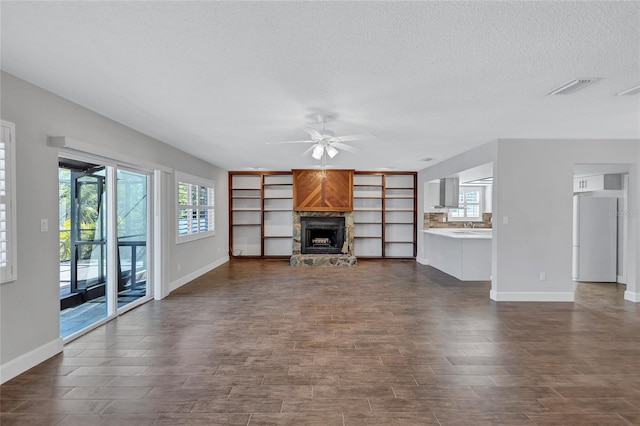 unfurnished living room with ceiling fan, a stone fireplace, and a textured ceiling