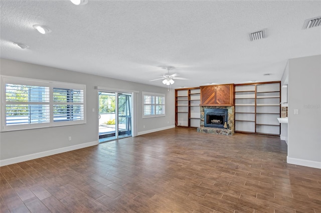 unfurnished living room featuring ceiling fan, a fireplace, dark hardwood / wood-style flooring, and a textured ceiling