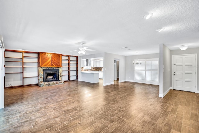 unfurnished living room featuring a textured ceiling, a stone fireplace, wood-type flooring, and ceiling fan with notable chandelier