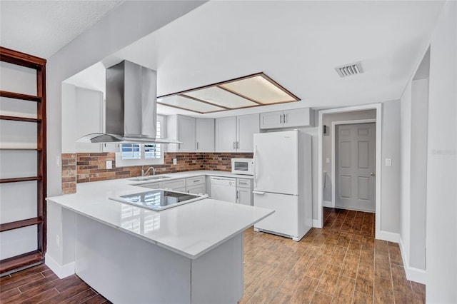 kitchen featuring island exhaust hood, kitchen peninsula, white appliances, sink, and wood-type flooring