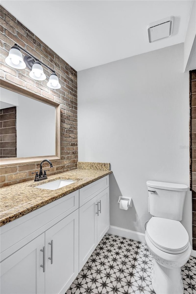 bathroom featuring toilet, vanity, tile patterned floors, and brick wall