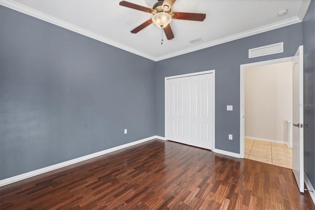 unfurnished bedroom featuring baseboards, visible vents, ornamental molding, dark wood-type flooring, and a closet