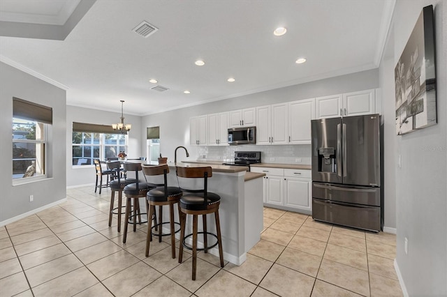 kitchen with a center island with sink, stainless steel appliances, visible vents, hanging light fixtures, and white cabinetry