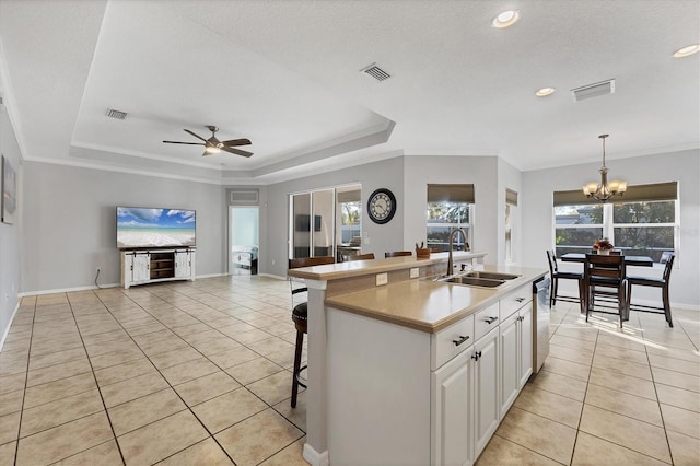 kitchen featuring white cabinets, hanging light fixtures, a kitchen island with sink, a tray ceiling, and a sink