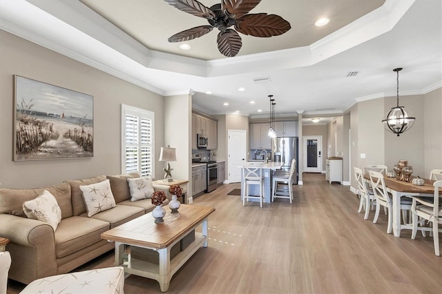 living room featuring a tray ceiling, light hardwood / wood-style flooring, and ornamental molding