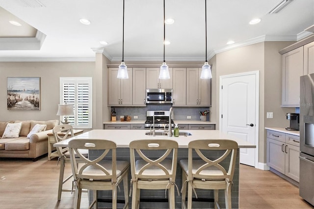 kitchen with sink, stainless steel appliances, an island with sink, decorative light fixtures, and light wood-type flooring