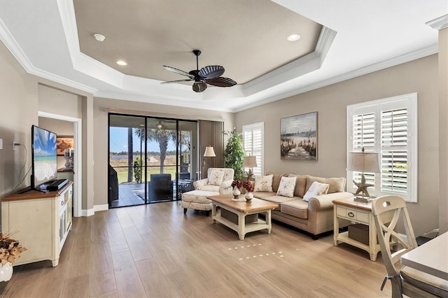 living room with ceiling fan, a raised ceiling, ornamental molding, and light hardwood / wood-style flooring