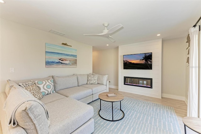 living room with a large fireplace, light hardwood / wood-style floors, and ceiling fan