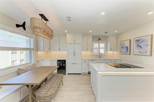 kitchen featuring black electric cooktop, white cabinetry, white dishwasher, and decorative light fixtures