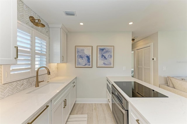 kitchen featuring black electric stovetop, oven, sink, light hardwood / wood-style flooring, and light stone counters