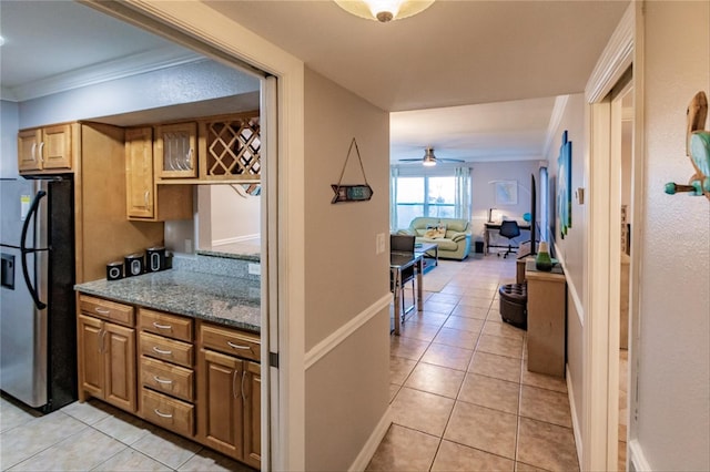 kitchen featuring light stone countertops, stainless steel fridge, ornamental molding, ceiling fan, and light tile patterned floors