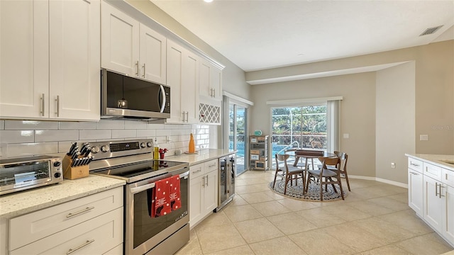 kitchen with light stone counters, backsplash, appliances with stainless steel finishes, and white cabinetry