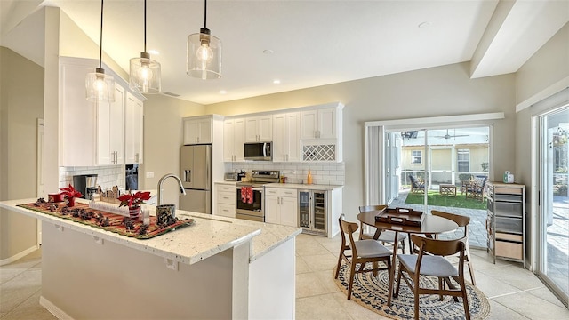 kitchen featuring hanging light fixtures, white cabinets, light stone counters, light tile patterned flooring, and stainless steel appliances