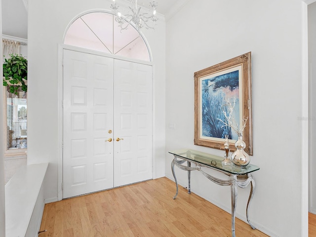 entryway featuring wood-type flooring, crown molding, and a notable chandelier