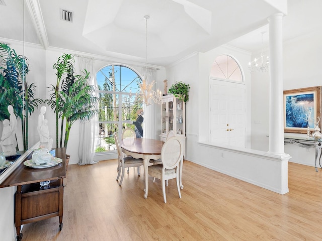 dining space featuring a notable chandelier, light wood-type flooring, ornate columns, and crown molding