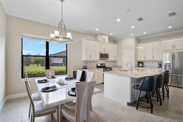 kitchen featuring a kitchen island with sink, sink, appliances with stainless steel finishes, decorative light fixtures, and white cabinetry