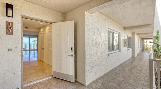 corridor featuring a healthy amount of sunlight, a textured wall, visible vents, and a textured ceiling