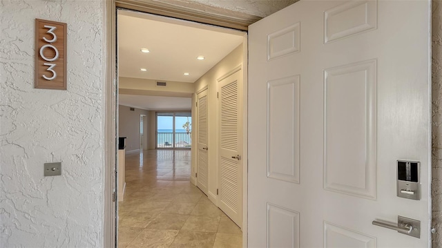 hallway featuring light tile patterned flooring, baseboards, visible vents, and a textured wall