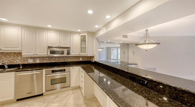 kitchen with appliances with stainless steel finishes, white cabinets, glass insert cabinets, and dark stone countertops