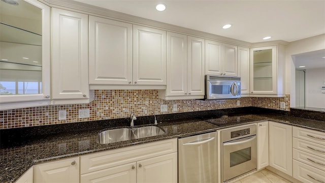 kitchen with appliances with stainless steel finishes, dark stone counters, glass insert cabinets, and a sink