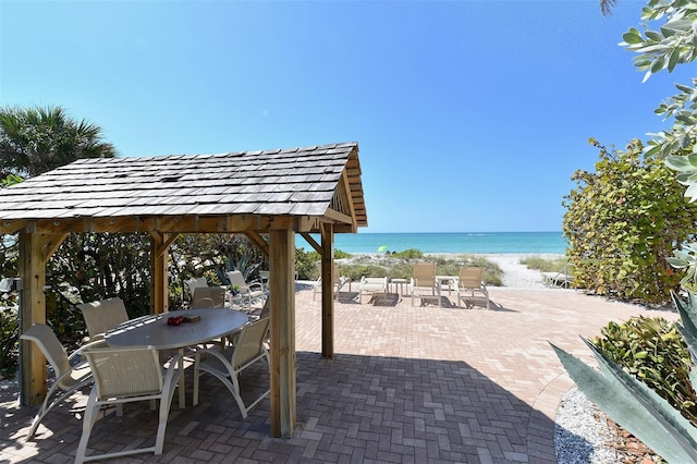 view of patio / terrace featuring a beach view, outdoor dining space, and a water view