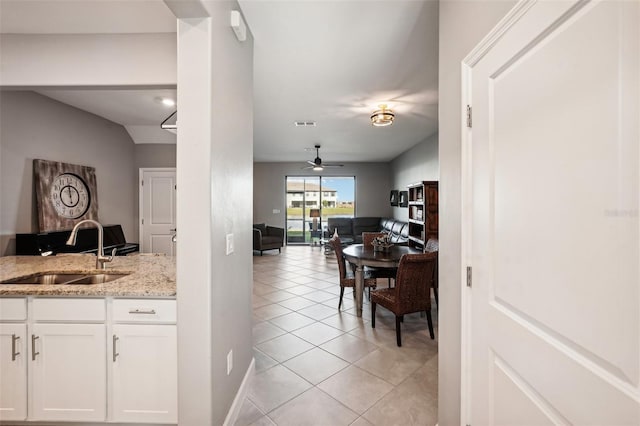 kitchen featuring ceiling fan, sink, light tile patterned floors, light stone counters, and white cabinets