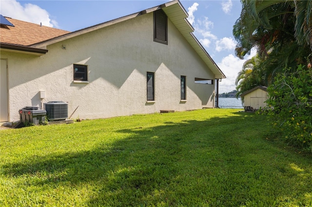 exterior space featuring a lawn, central AC unit, a water view, and a shed