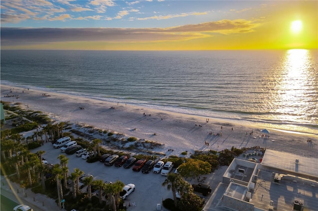 aerial view at dusk featuring a water view and a beach view