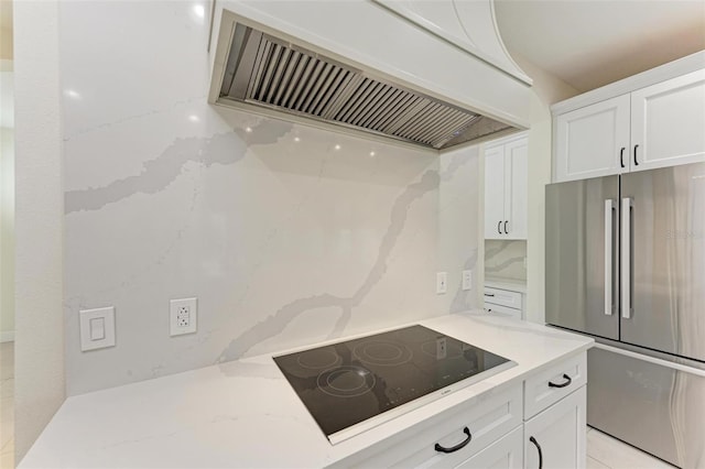 kitchen featuring decorative backsplash, black electric stovetop, premium range hood, white cabinets, and stainless steel refrigerator