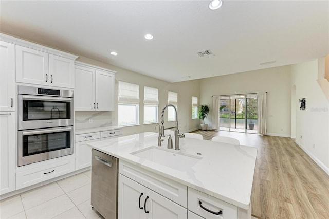 kitchen with a kitchen island with sink, white cabinets, sink, light wood-type flooring, and stainless steel appliances