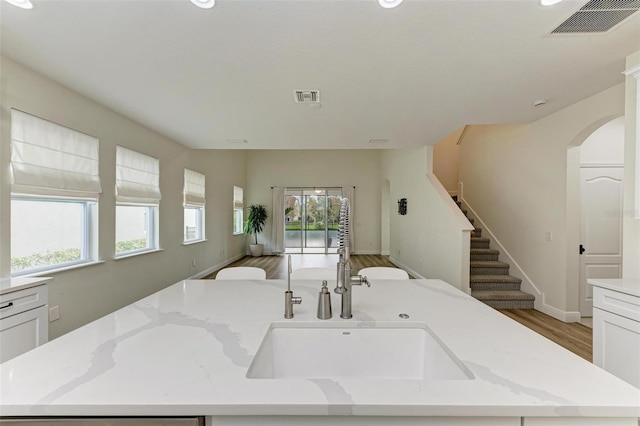 kitchen featuring a wealth of natural light, light stone counters, a kitchen island with sink, and wood-type flooring