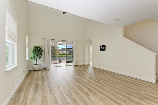 unfurnished living room with light wood-type flooring and a towering ceiling