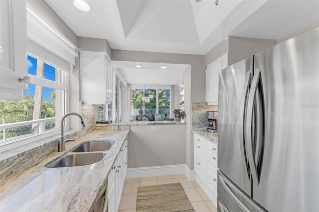 kitchen featuring white cabinets, sink, decorative backsplash, light stone counters, and stainless steel refrigerator