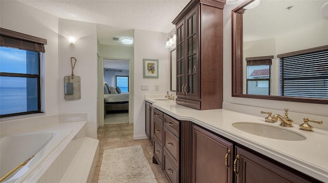 bathroom with vanity, tile patterned flooring, a textured ceiling, and tiled tub