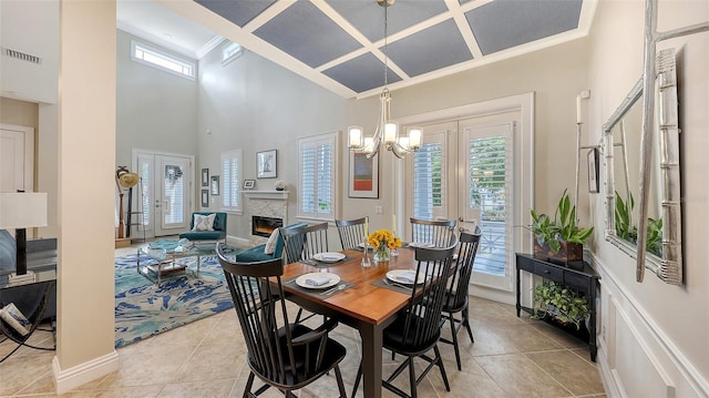 tiled dining room with a chandelier, a towering ceiling, a stone fireplace, and french doors