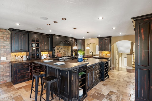 8855 Midnight Pass Rd, Sarasota, FL 34242 - kitchen featuring arched walkways, a center island with sink, tasteful backsplash, a sink, and stone tile floors