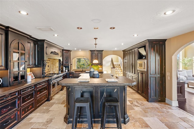 kitchen with a kitchen breakfast bar, premium range hood, decorative light fixtures, a kitchen island, and appliances with stainless steel finishes