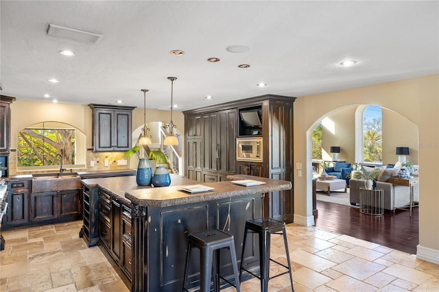 kitchen featuring a center island, backsplash, hanging light fixtures, dark brown cabinetry, and a breakfast bar area