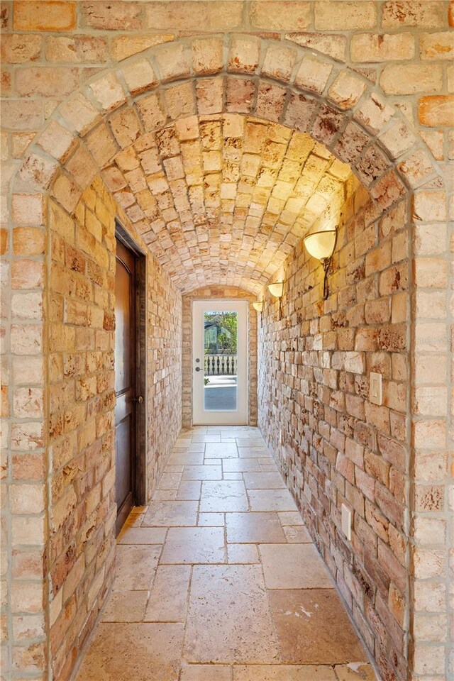 hallway with brick ceiling, brick wall, and vaulted ceiling