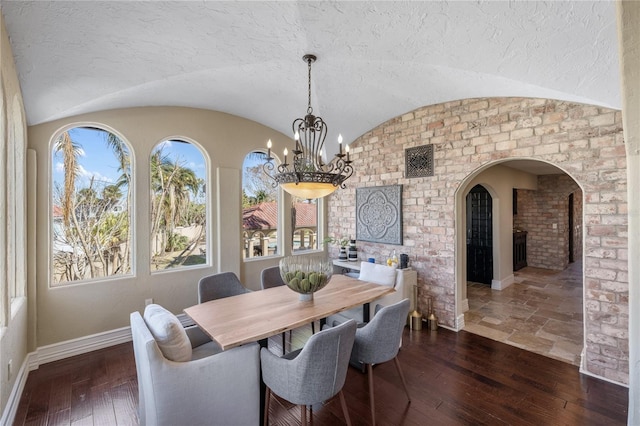 dining space with dark hardwood / wood-style floors, lofted ceiling, a textured ceiling, and an inviting chandelier