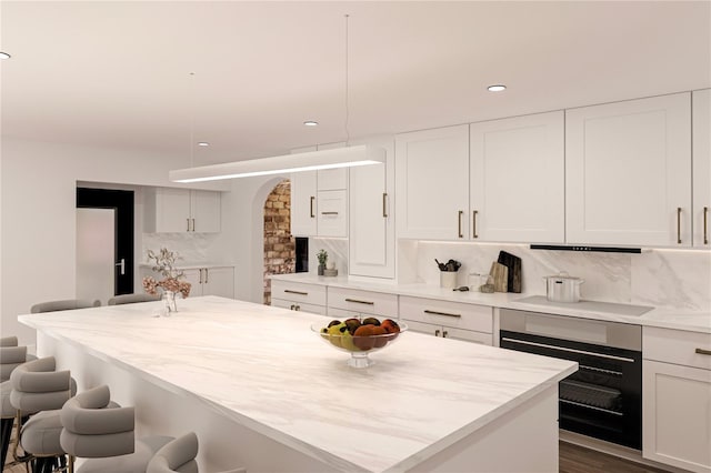 kitchen with stainless steel oven, decorative light fixtures, stovetop, white cabinetry, and a breakfast bar area