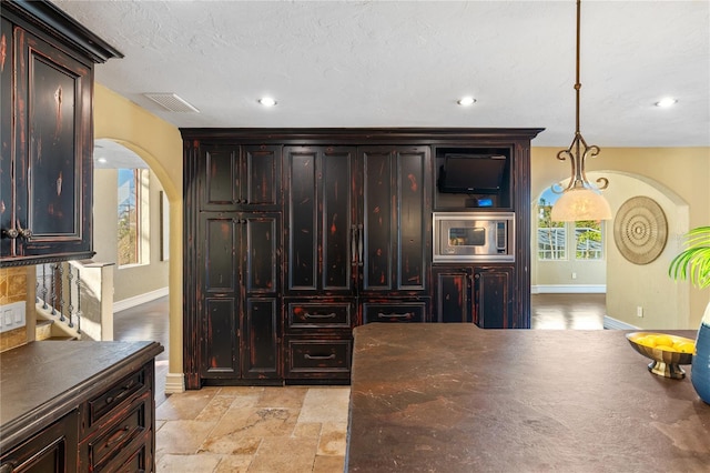 bar featuring pendant lighting, dark brown cabinets, a textured ceiling, and stainless steel microwave