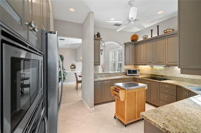 kitchen featuring ceiling fan, appliances with stainless steel finishes, decorative backsplash, a kitchen island, and light stone counters