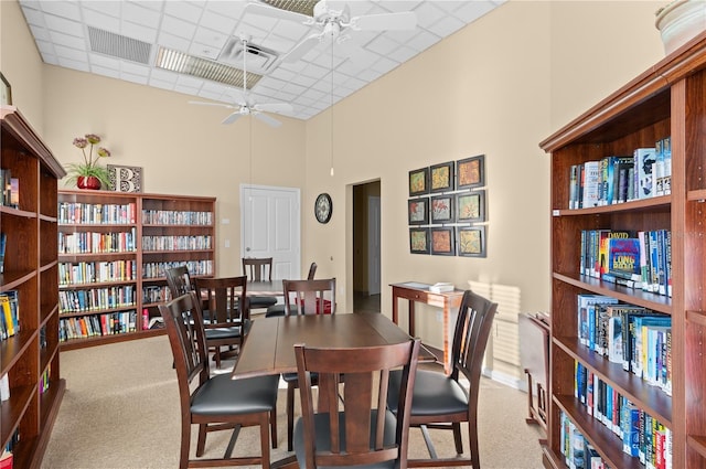 dining space featuring ceiling fan, carpet flooring, a paneled ceiling, and a high ceiling