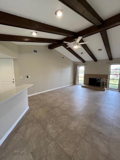 unfurnished living room featuring ceiling fan and vaulted ceiling with beams